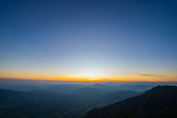 A breathtaking sunset over layered mountain ranges, with warm golden light fading into a deep blue sky, creating a serene and expansive natural landscape ideal for travel and nature themes. © Narong Niemhom