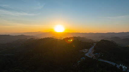 Fototapeta premium Golden sunset light glowing over a winding mountain road on a high ridge in Nan Province, Thailand, creating a dramatic landscape of curves, peaks, and warm evening atmosphere.