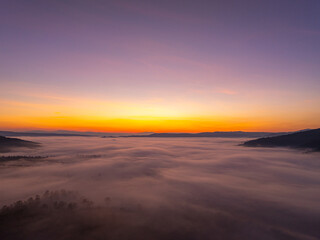 An aerial cinematic sunrise showcasing vibrant sky colors above a fog-covered valley, creating a serene and inspiring nature travel atmosphere. Brilliant Sunrise Painting the Sky Over the Valley