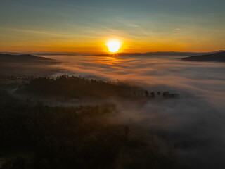 Fototapeta premium Drone footage capturing a peaceful morning scene as sunlight breaks through clouds and fog, revealing layered mountains and a vast natural landscape at dawn.