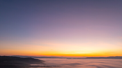 Obraz premium A stunning aerial landscape of sunrise over mountains wrapped in soft fog, perfect for travel, nature, and cinematic visual storytelling. Vibrant Sunrise Over a Tranquil Valley Wrapped in Morning Fog