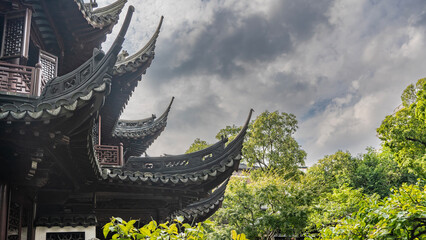 Details of Chinese architecture. The roof of the building has carved curved cornice edges. The background is green vegetation, clouds in the sky. China. Shanghai. © Вера 