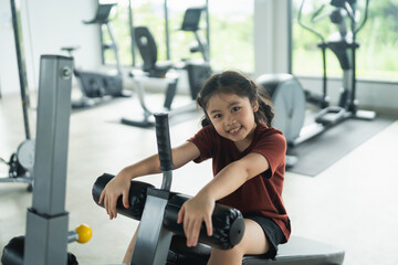 Fototapeta premium Young Girl Enjoys Fitness Routine in Modern Gym, Smiling and Engaging with Exercise Equipment, Promoting Health and Active Lifestyle for Children