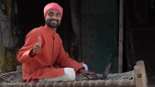 Indian farmer using laptop  and showing thumps up at home