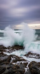 Obraz premium Powerful ocean waves driven by a strong gale crash against a rocky shoreline under a moody, overcast sky, emphasizing the raw force of nature, untamed, nature, foam