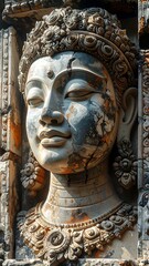 Obraz premium Close-up of a weathered stone carving, showing the serene face of a deity with intricate headwear, detailed facial features, and partial erosion
