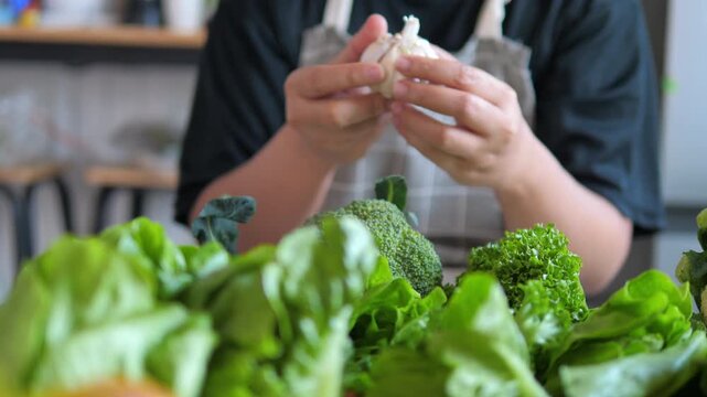 Person preparing fresh vegetables with garlic on kitchen table. Home cooking, healthy meal preparation and clean eating concept