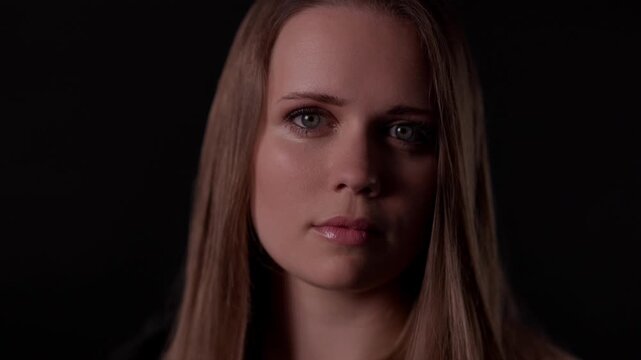 Portrait of a young Caucasian woman with long brown hair looking down, feeling sad and pensive on a dark background