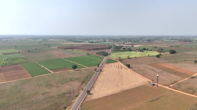 Drone aerial view of rural farmland with country road crossing agricultural fields. Countryside landscape showing agriculture