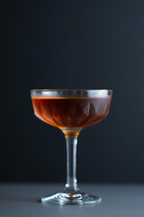 A chilled glass containing a dark amber alcoholic cocktail sits on a table with a dark background