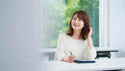 窓際でペンを持ち髪を触りながらアイデアを練る女性