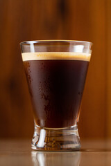 A refreshing cold glass of iced coffee with rich creamy foam sits on a wooden table surface