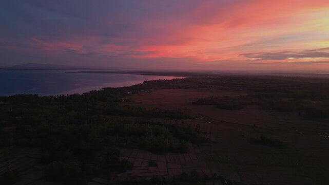Diagonal aerial angle capturing rice fields and winding road in Tondol glowing under a dramatic sunset sky.