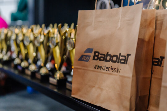 Babolat branded paper bags placed beside golden trophies on a table at a padel tournament event showcasing awards