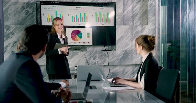 Caucasian businesswoman holding tablet while presenting marketing report to multiracial colleagues in professional office setting during strategic team meeting and communication planning