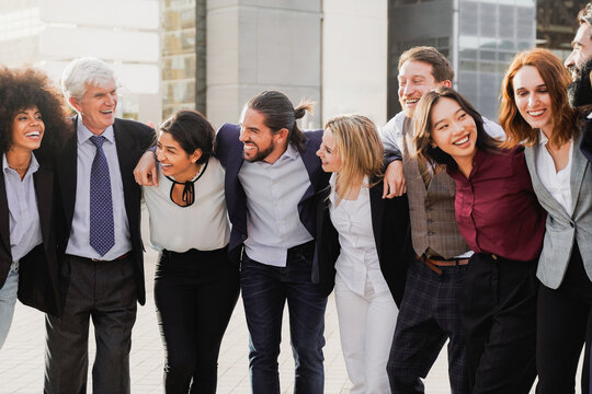 Group of multigenerational business celebrating and hug with office buildings on background - Businesspeople with diverse age and ethnicity concept