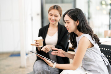 Fototapeta premium Two professional Asian businesswomen collaborating on a digital tablet and sharing ideas during a productive meeting in a modern office environment.