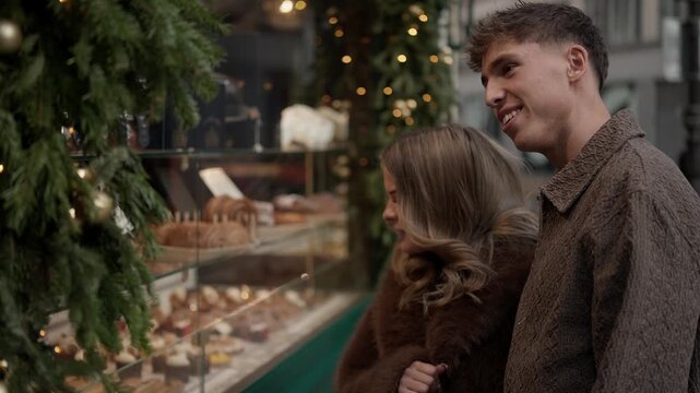 A young couple in Paris France window shopping at a bakery during the Christmas season The exterior shot showcases a patisserie with a display of cakes and pastries.