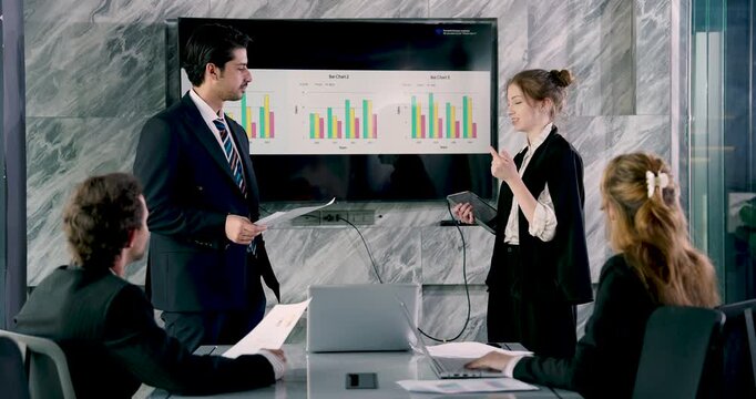 Business team discussing bar chart presentation while standing executives reviewing report content together in formal office meeting for strategic collaboration and data-driven planning