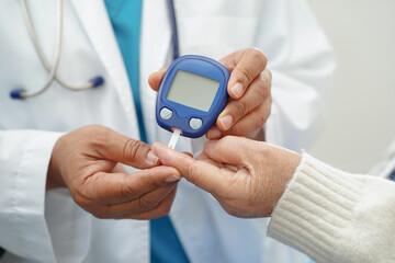 Asian doctor using digital glucose meter for check sample blood sugar level to treatment diabetes.