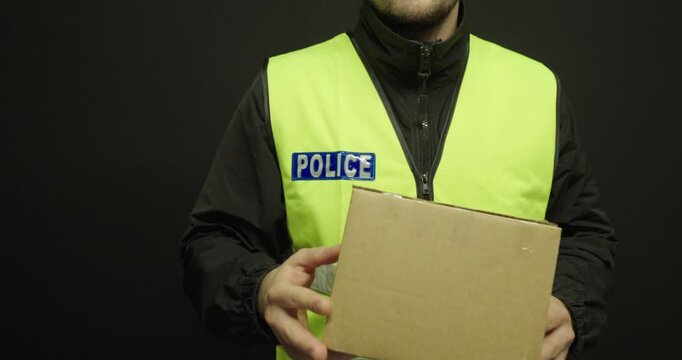 police officer wearing a safety vest while holding a suspicious package against a dark background. Concept of security, threat assessment, law enforcement, and public safety.