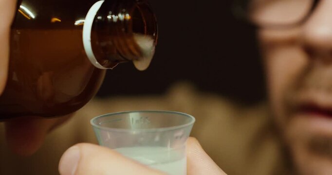 Close-up of a man carefully pouring liquid medicine from a bottle into a measuring cup. Concept of correct dosage, medication safety, healthcare routine, and treatment preparation.