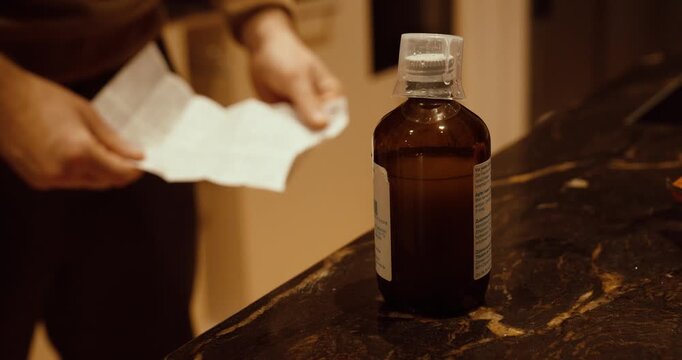 Medicine bottle on a kitchen counter while a person reads the package leaflet. Concept of medication safety, correct usage, dosage instructions, and healthcare awareness.