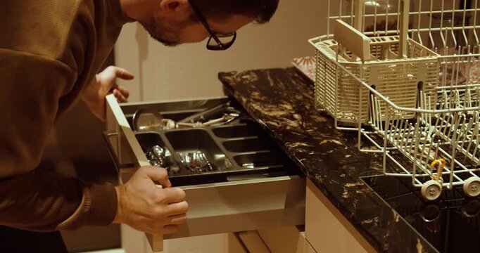 Close-up of a man fixing a jammed kitchen drawer near a dishwasher. Concept of household repair, furniture maintenance, and domestic problem solving.