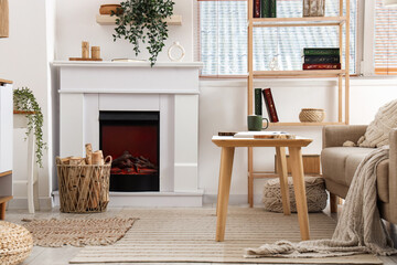 Naklejka premium Interior of living room with sofa, shelving unit, coffee table, fireplace, houseplants and firewood in wicker basket