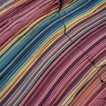 Sedimentary rock layers dramatically folded and bent by immense geological pressure. A close view of ancient, multicolored strata, surface, detail, earth