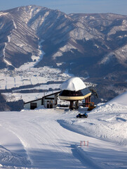 Sunny ski slope featuring a lift terminal and snowmobile with village view below