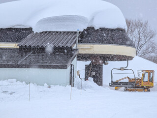 Yellow snowcat parked beneath a snow-laden ski lift terminal during a storm
