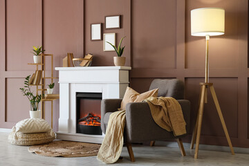 Naklejka premium Interior of cozy living room with grey armchair, glowing lamp and stylish fireplace