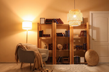 Interior of stylish living room with grey armchair, glowing lamps and bookshelves at evening © Pixel-Shot