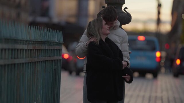 A romantic couple embraces on a bridge in Paris France at dusk The scene features soft focus and shallow depth of field with cars passing by in the background The couple is seen in a loving embrace sh