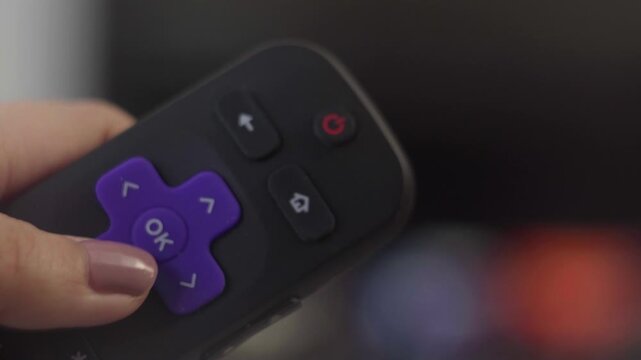 Woman's hand pressing ok button on a smart tv remote for streaming media services and home entertainment