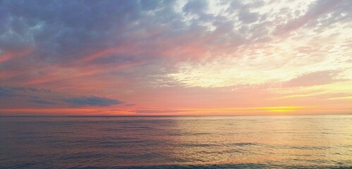 Obraz premium A vibrant sunset over a calm sea, featuring a dramatic sky filled with pink, orange, and blue clouds reflecting on the gentle waves.