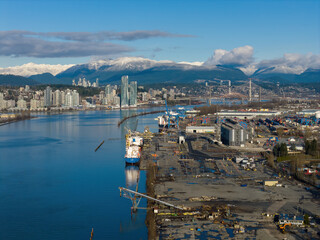 Obraz premium Industrial Port View Of Fraser River With Snowy Mountains, Modern City Skyline, And Cargo Yard