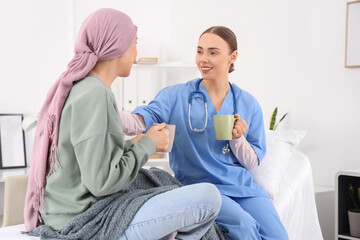 Obraz premium Mature woman after chemotherapy with nurse drinking tea in hospital room. Brain cancer concept