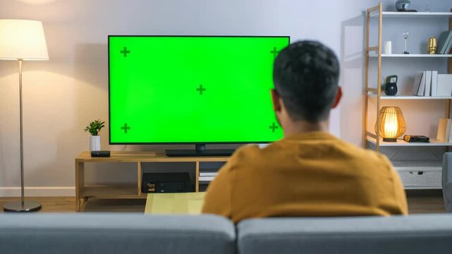 Man sitting on sofa watching large green screen television in living room