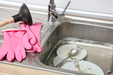 Metallic sink with soap water, rubber gloves and plunger in kitchen, closeup