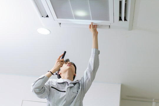 天井埋め込み型エアコンの点検をする若い日本人男性