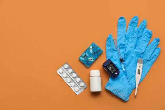 Pulse oximeter, blister pack of pills, rubber gloves, thermometer and syringe on beige background