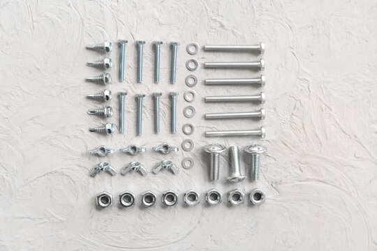 Arrangement of different tap bolts and chrome nuts on white grunge background