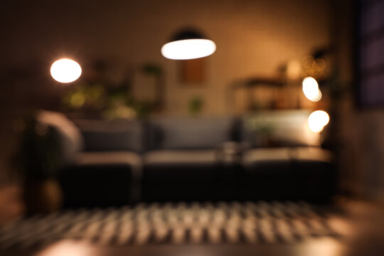 Interior of dark living room with comfortable sofa, coffee table and glowing lamps. Blurred view
