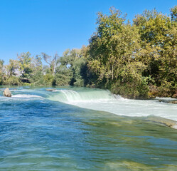 Panoramic view of the famous Manavgat Waterfall near Side with emerald water and lush green trees.