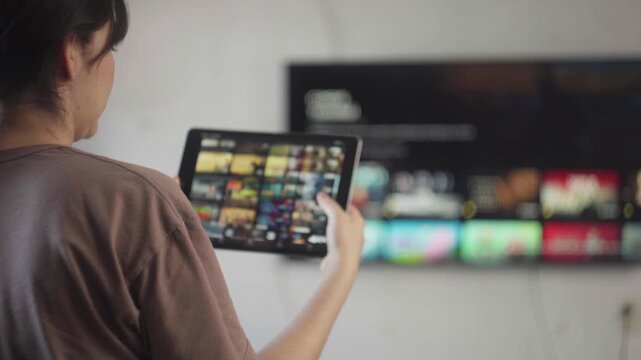 Woman streaming video on demand content using a tablet and smart tv for entertainment at home