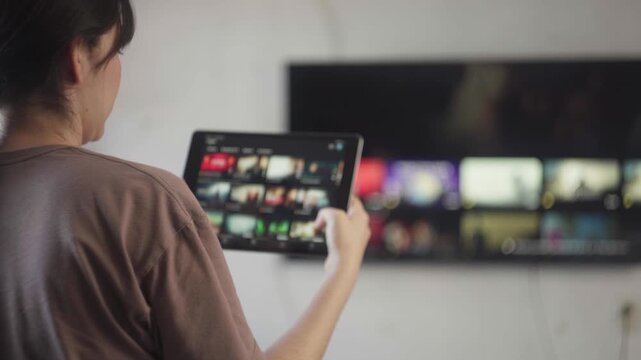 Woman streaming video on demand on a smart tv using a tablet for media consumption and entertainment