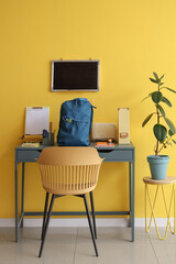 Workspace with school supplies, blank chalkboard and backpack near yellow wall