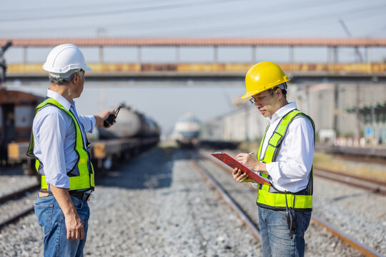 Railway engineers coordinating inspection and safety checks at a rail yard with tanker trains in the background. Concept of rail operations, teamwork